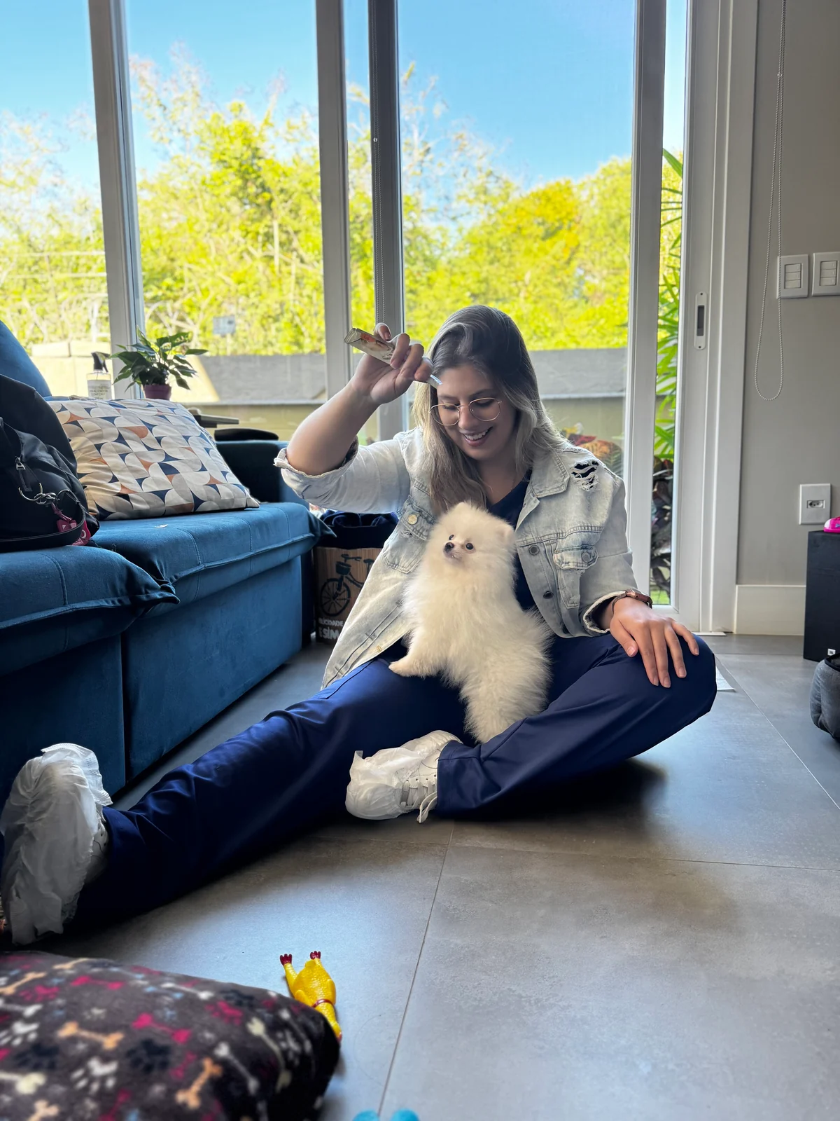 Ratiba Baja sentada no chão de uma sala com um cão pequeno no colo