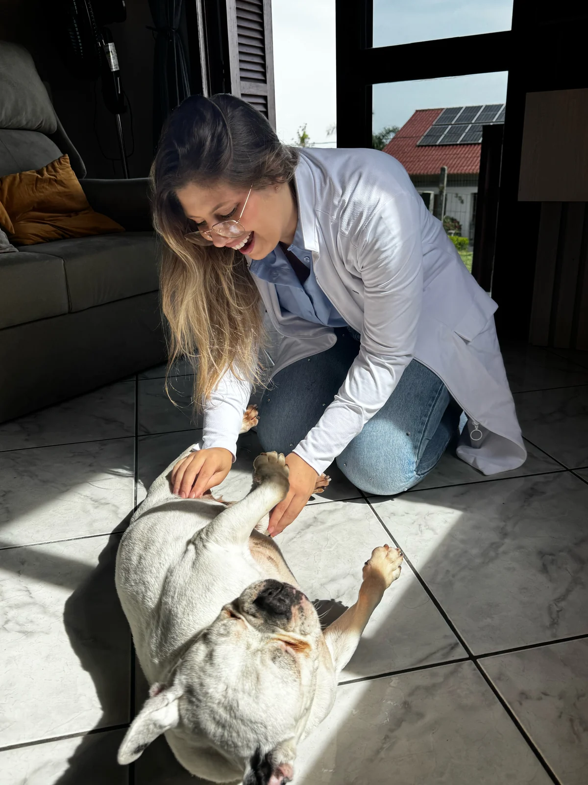 Ratiba Baja de jaleco com um cão deitado de barriga para cima em casa